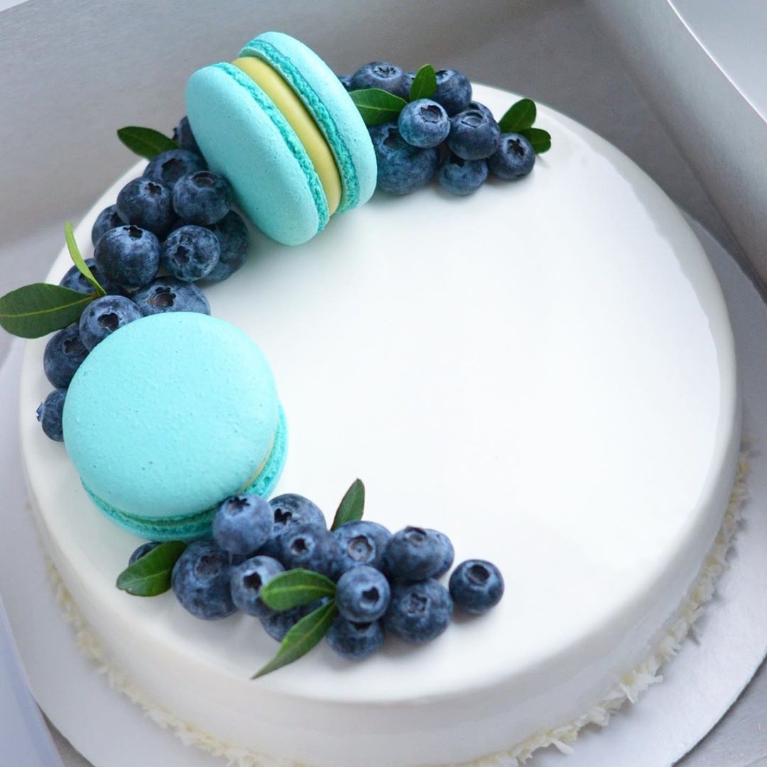 Круглый торт с покрытием гляссаж белого цвета, пирожными макарон и голубикой